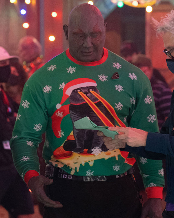 Drax wearing a green Christmas sweater with a penguin design in a festive setting.