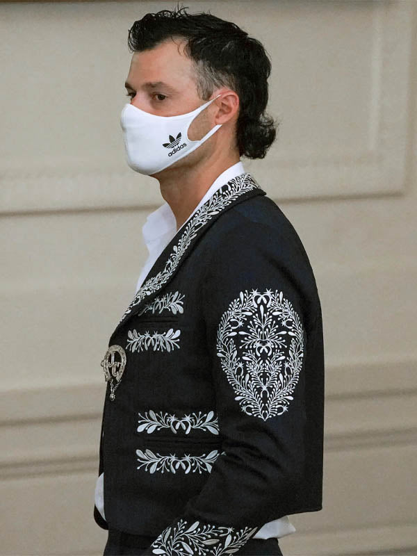 Person wearing a black embroidered jacket and white face mask with Adidas logo.