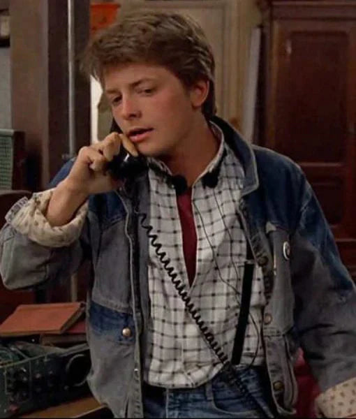 Person in a plaid shirt and denim jacket talking on a phone in an indoor setting