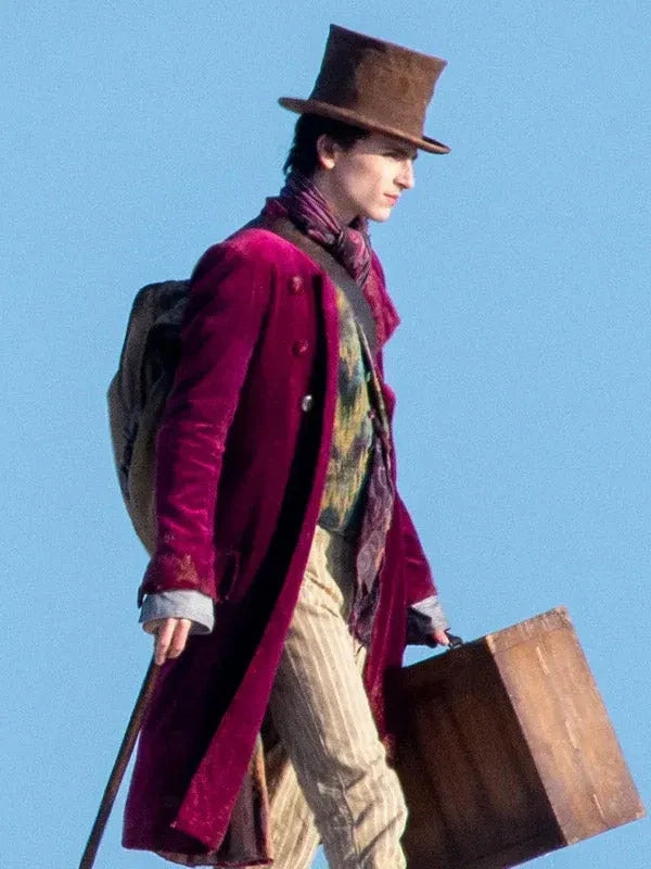 Person in vintage attire with a top hat, long coat, and suitcase against a clear blue sky.