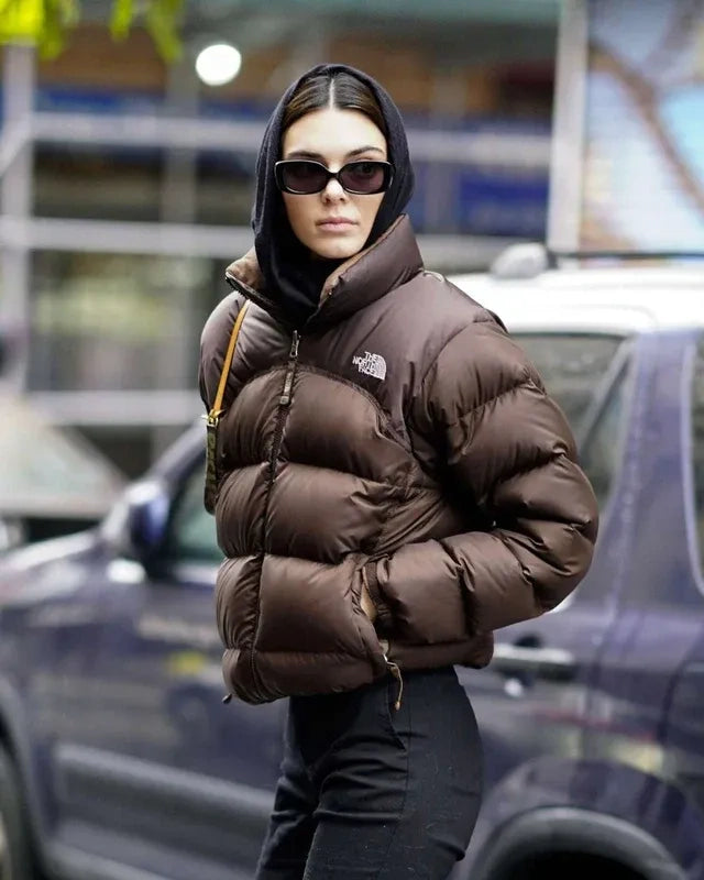 Person wearing a brown puffer jacket with 'The North Face' logo in an urban setting.