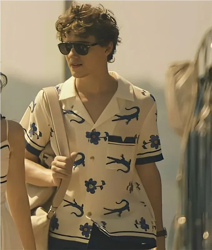 Person wearing a patterned shirt with sunglasses and a beige bag in an indoor setting